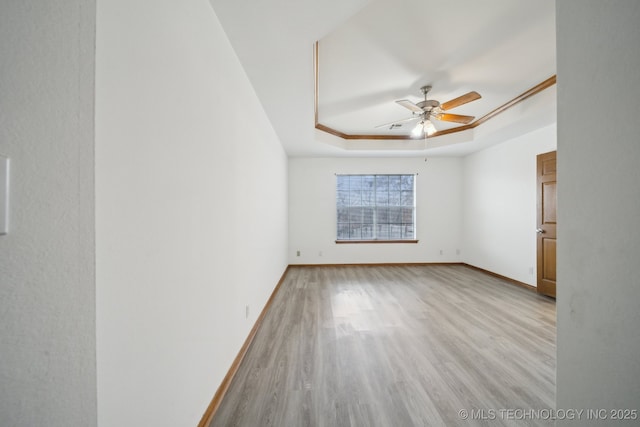 unfurnished room featuring a raised ceiling, ceiling fan, and light hardwood / wood-style flooring