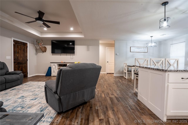 living room with dark wood-type flooring, ceiling fan, and a raised ceiling