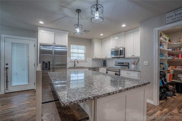 kitchen with white cabinetry, stainless steel appliances, decorative light fixtures, and a kitchen island