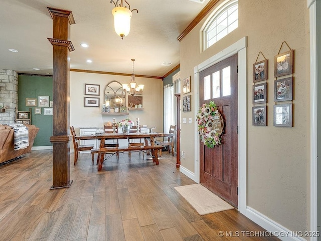 foyer featuring ornate columns, crown molding, hardwood / wood-style floors, and an inviting chandelier