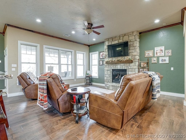 living room with ceiling fan, hardwood / wood-style floors, a fireplace, ornamental molding, and a textured ceiling