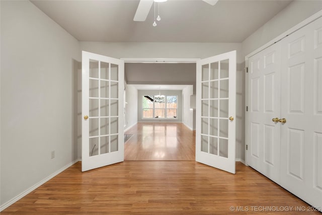 empty room with hardwood / wood-style flooring, ceiling fan with notable chandelier, and french doors