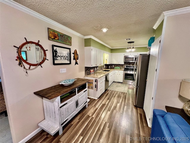 kitchen featuring appliances with stainless steel finishes, pendant lighting, white cabinets, decorative backsplash, and ornamental molding