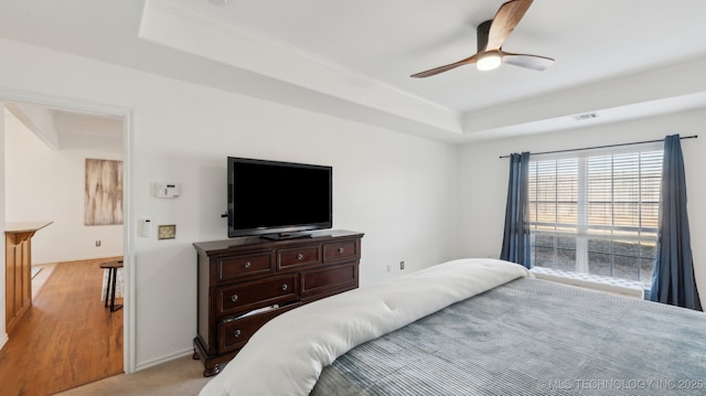 carpeted bedroom with a raised ceiling and ceiling fan