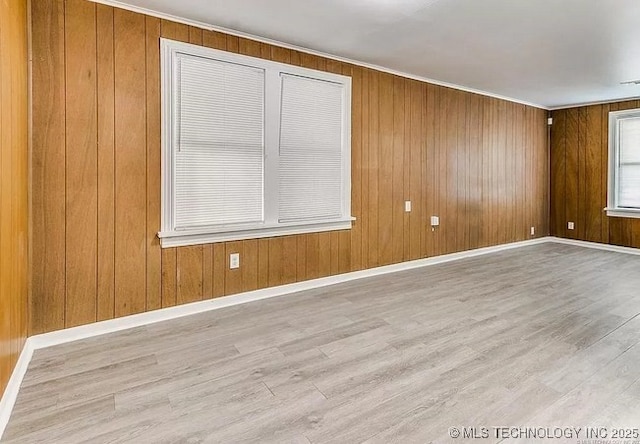 empty room with wood walls, ornamental molding, and light wood-type flooring