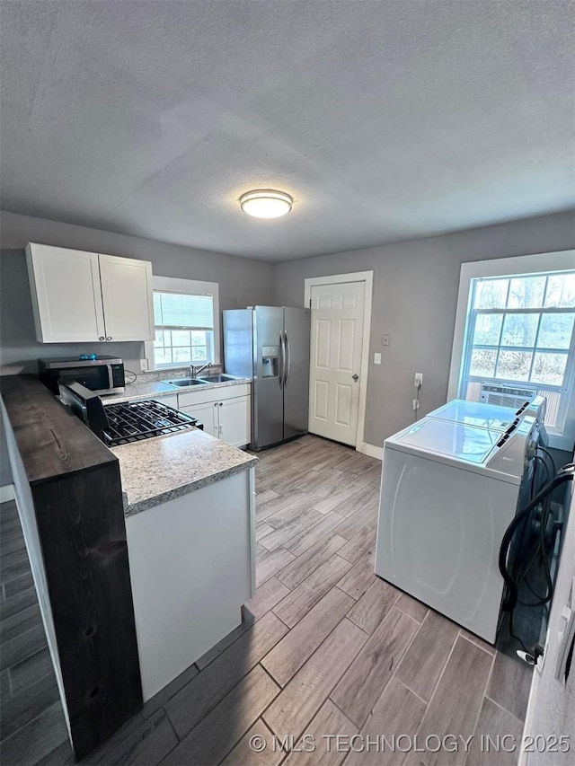 kitchen featuring sink, stainless steel appliances, washer and dryer, a textured ceiling, and white cabinets