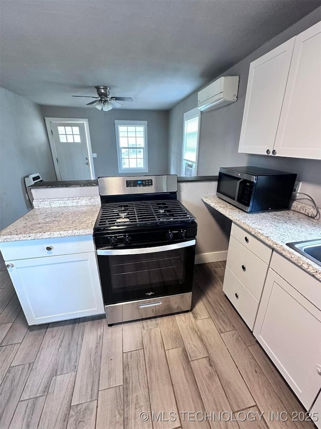 kitchen with light hardwood / wood-style floors, stainless steel appliances, an AC wall unit, and white cabinets