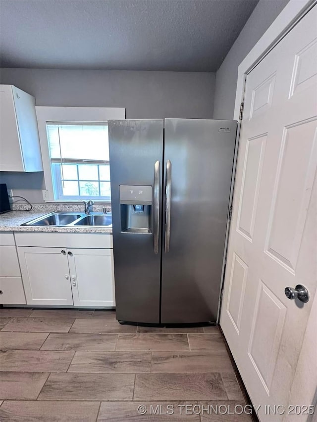 kitchen featuring white cabinetry, sink, stainless steel fridge, and a textured ceiling