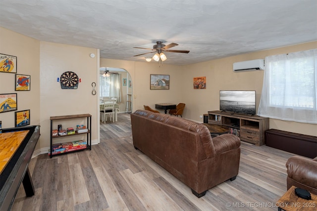 living room with ceiling fan, a wall mounted AC, light hardwood / wood-style flooring, and a wealth of natural light