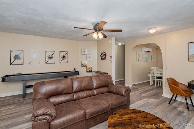 living room featuring a wall mounted air conditioner, a textured ceiling, wood-type flooring, and ceiling fan