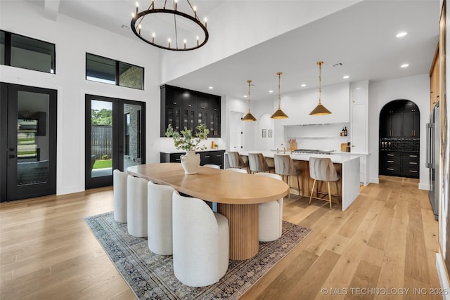 dining area with french doors, a towering ceiling, an inviting chandelier, and light wood-type flooring