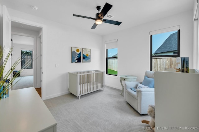 bedroom with ceiling fan, light colored carpet, and a crib