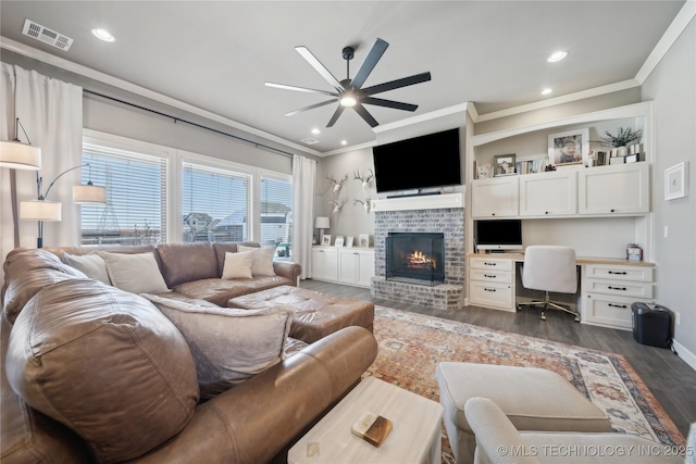 living room with ceiling fan, built in desk, ornamental molding, dark hardwood / wood-style flooring, and a brick fireplace