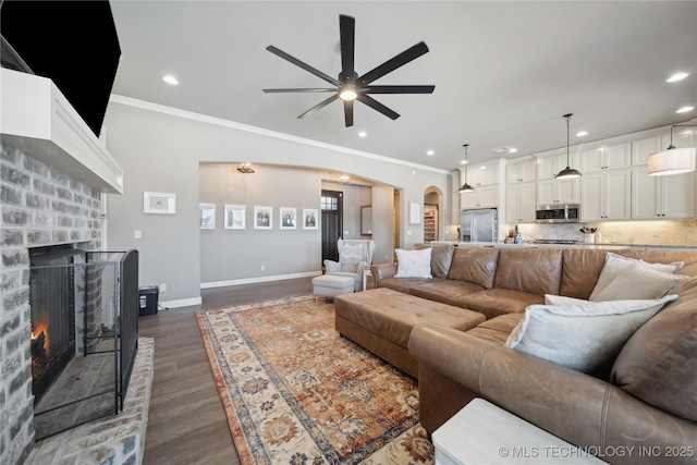 living room featuring dark hardwood / wood-style flooring, a brick fireplace, crown molding, and ceiling fan