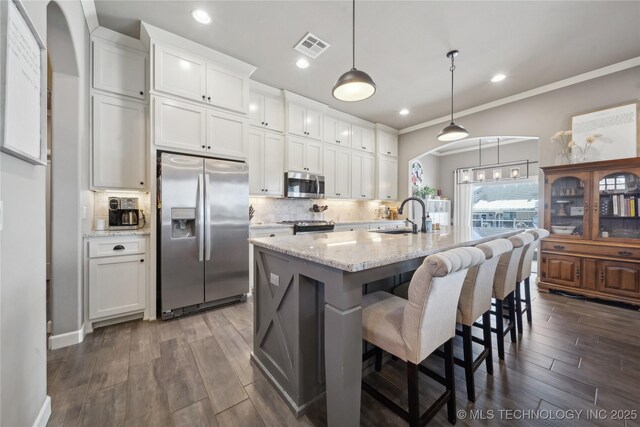 kitchen with a kitchen island with sink, hanging light fixtures, white cabinets, and appliances with stainless steel finishes