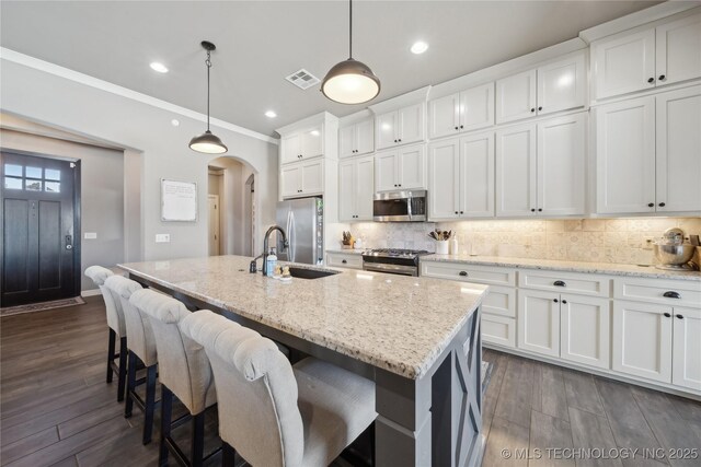 kitchen with appliances with stainless steel finishes, decorative light fixtures, and an island with sink