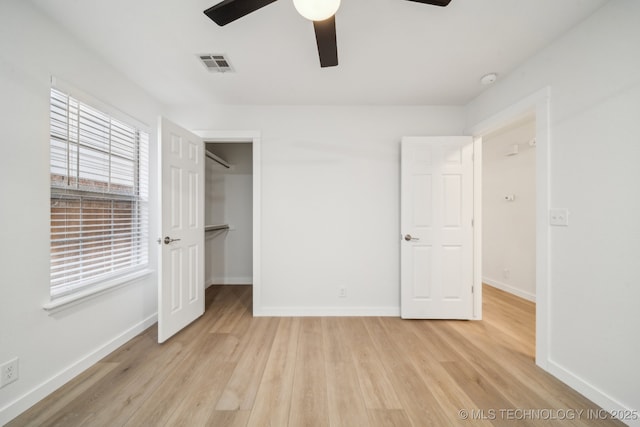 unfurnished bedroom with ceiling fan, a spacious closet, and light wood-type flooring