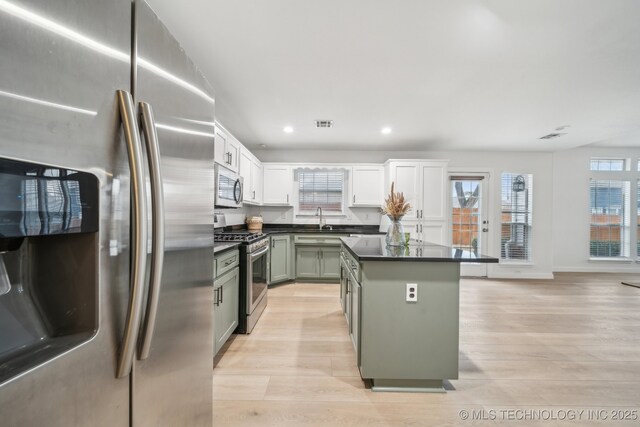 kitchen with appliances with stainless steel finishes, sink, white cabinets, a center island, and light hardwood / wood-style flooring