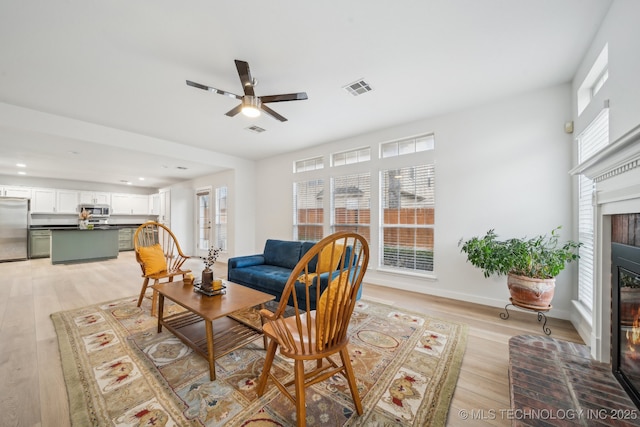 living room featuring a fireplace, ceiling fan, and light wood-type flooring