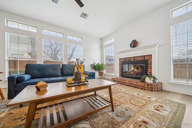 living room featuring ceiling fan, wood-type flooring, and a brick fireplace