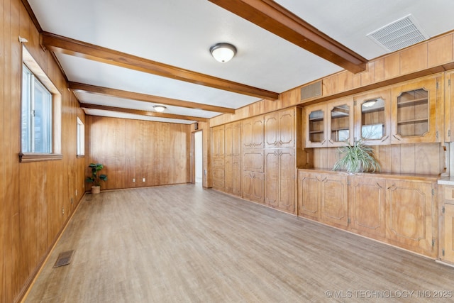 empty room featuring wood walls, light wood-style flooring, visible vents, and beam ceiling