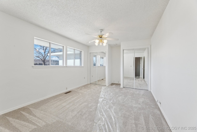 unfurnished bedroom with a textured ceiling, visible vents, multiple closets, and carpet flooring