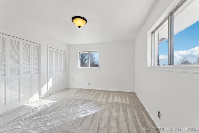 unfurnished bedroom featuring carpet floors, two closets, and baseboards