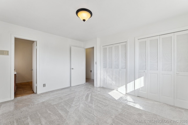 unfurnished bedroom featuring carpet, ensuite bath, and two closets