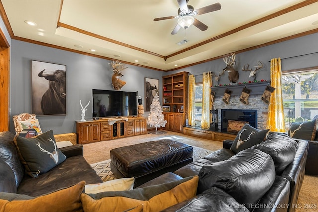 carpeted living room with crown molding, a tray ceiling, and a stone fireplace