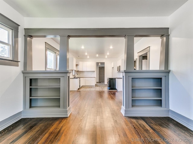 unfurnished living room featuring sink, dark wood-type flooring, and ornate columns