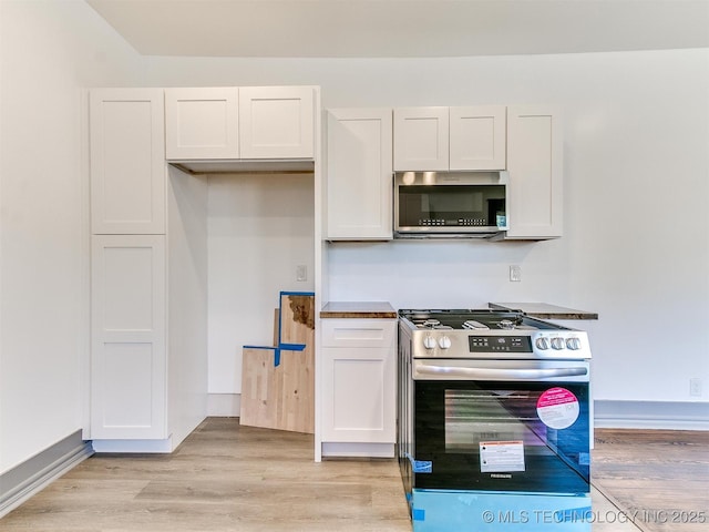 kitchen with stainless steel appliances, white cabinets, and light hardwood / wood-style floors