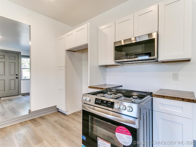 kitchen with stainless steel appliances, white cabinetry, butcher block countertops, and light hardwood / wood-style floors