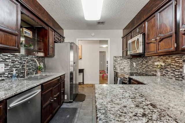 kitchen with sink, appliances with stainless steel finishes, dark brown cabinetry, light stone countertops, and decorative backsplash