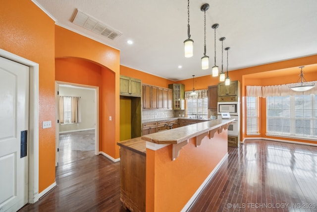 kitchen featuring white appliances, a breakfast bar area, hanging light fixtures, dark hardwood / wood-style flooring, and decorative backsplash