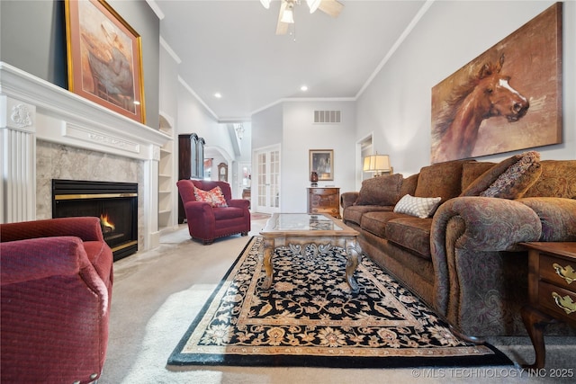 living room featuring built in features, a premium fireplace, ceiling fan, ornamental molding, and light carpet