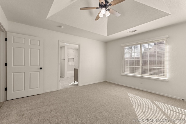 unfurnished bedroom with ceiling fan, connected bathroom, a raised ceiling, and light carpet