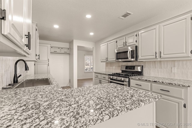 kitchen featuring appliances with stainless steel finishes, tasteful backsplash, sink, white cabinets, and a textured ceiling