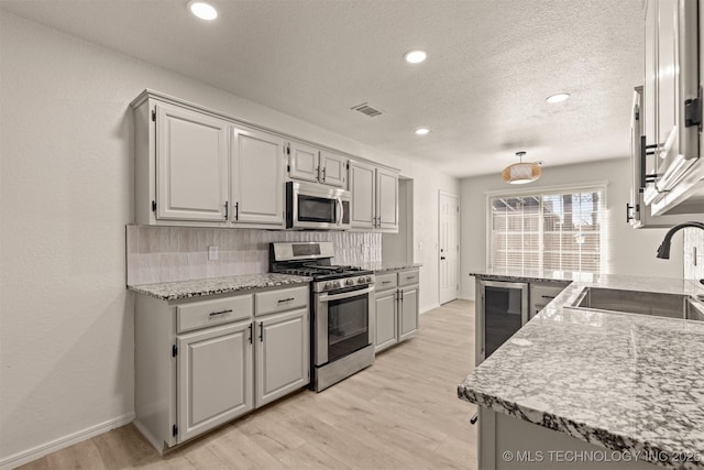 kitchen featuring appliances with stainless steel finishes, sink, wine cooler, decorative backsplash, and light hardwood / wood-style floors