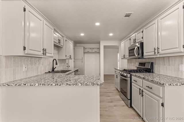 kitchen with appliances with stainless steel finishes, white cabinetry, sink, a textured ceiling, and light hardwood / wood-style flooring