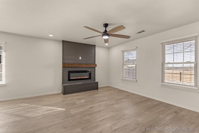 unfurnished living room featuring ceiling fan, a textured ceiling, a fireplace, and light hardwood / wood-style floors