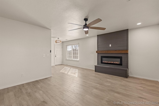 unfurnished living room with a textured ceiling, light hardwood / wood-style flooring, a large fireplace, and ceiling fan