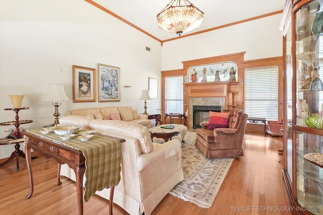 living room featuring crown molding, high vaulted ceiling, light hardwood / wood-style floors, and a tile fireplace