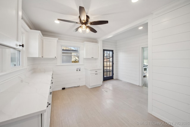 kitchen with light stone countertops, white cabinets, ceiling fan, and wood walls