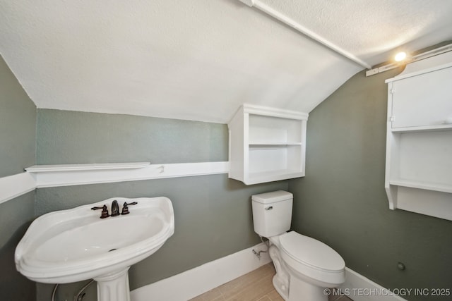 bathroom with lofted ceiling, toilet, sink, and a textured ceiling