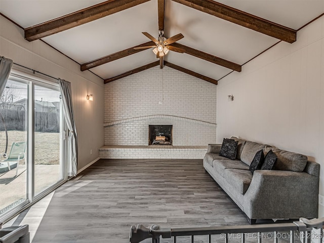 living room featuring vaulted ceiling with beams, wood-type flooring, a brick fireplace, ceiling fan, and brick wall