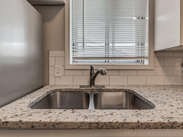 kitchen with light stone counters, sink, and backsplash