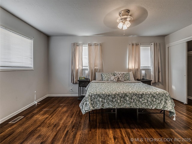 bedroom with dark wood-type flooring, a textured ceiling, ceiling fan, and a closet