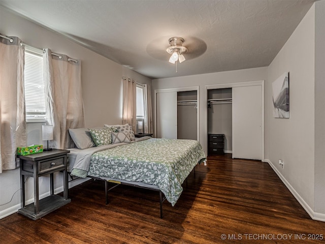 bedroom featuring multiple windows, two closets, dark hardwood / wood-style floors, and ceiling fan