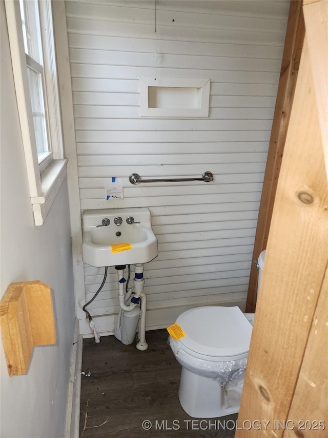 bathroom with wooden walls, wood-type flooring, toilet, and sink