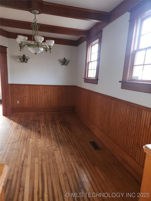 spare room with beamed ceiling, hardwood / wood-style flooring, wooden walls, and a chandelier